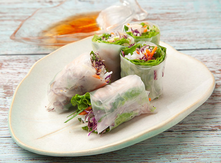 Fresh spring rolls served on a plate. Fresh rolls feature a mix of herbs, vegetables, rice noodles, and often shrimp or pork, wrapped in softened rice paper and served cold with a dipping sauce like peanut sauce or nuoc cham.